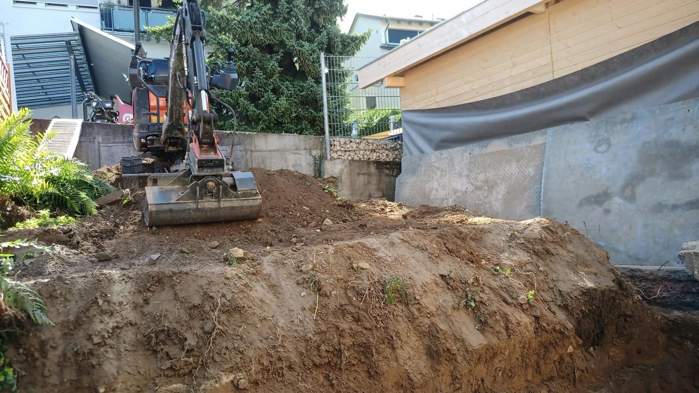 Minibagger modelliert den Erdaushub vor der Betonstützwand