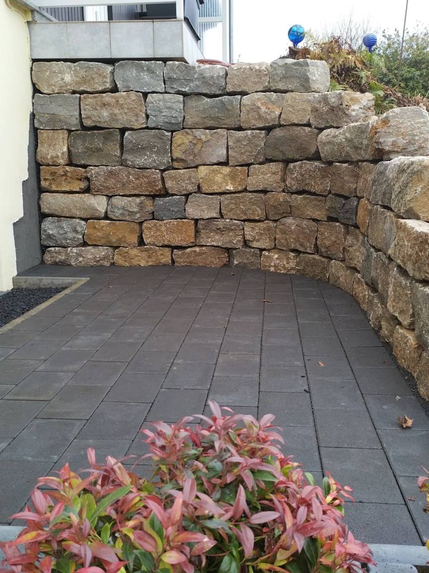 Natursteinmauer aus Bruchsteinen neben der Plattenterrasse