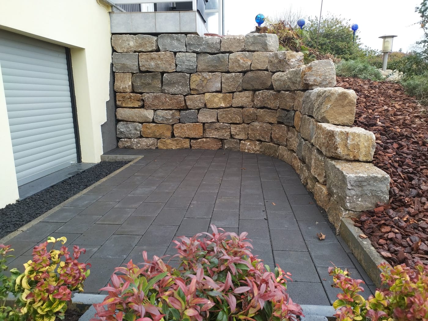 Natursteinmauer aus Bruchsteinen am gepflasterten Garagenzugang