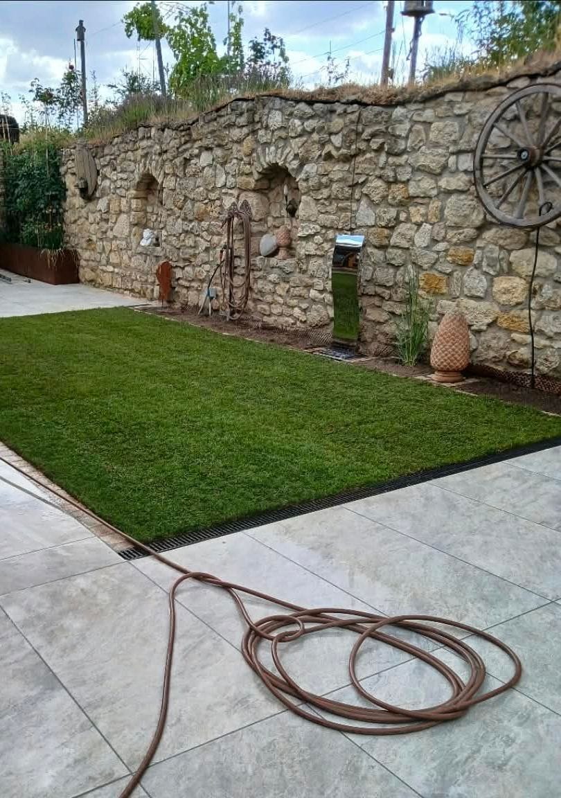Neu verlegter Rollrasen zwischen Terrassenplatten und Natursteinmauer